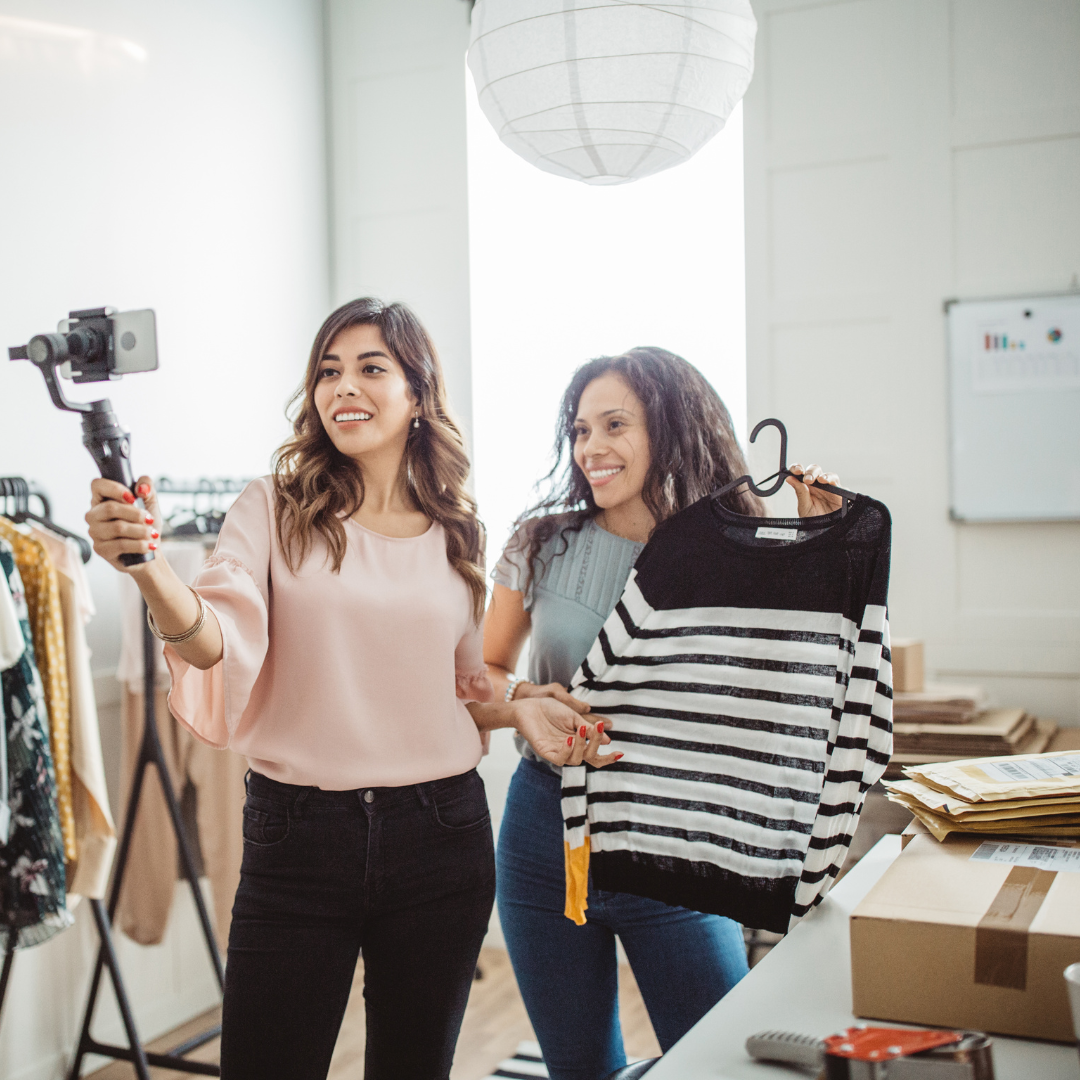 Two small business owners wearing caasual clothing, taking pictures of the new arrivals of their retail store.